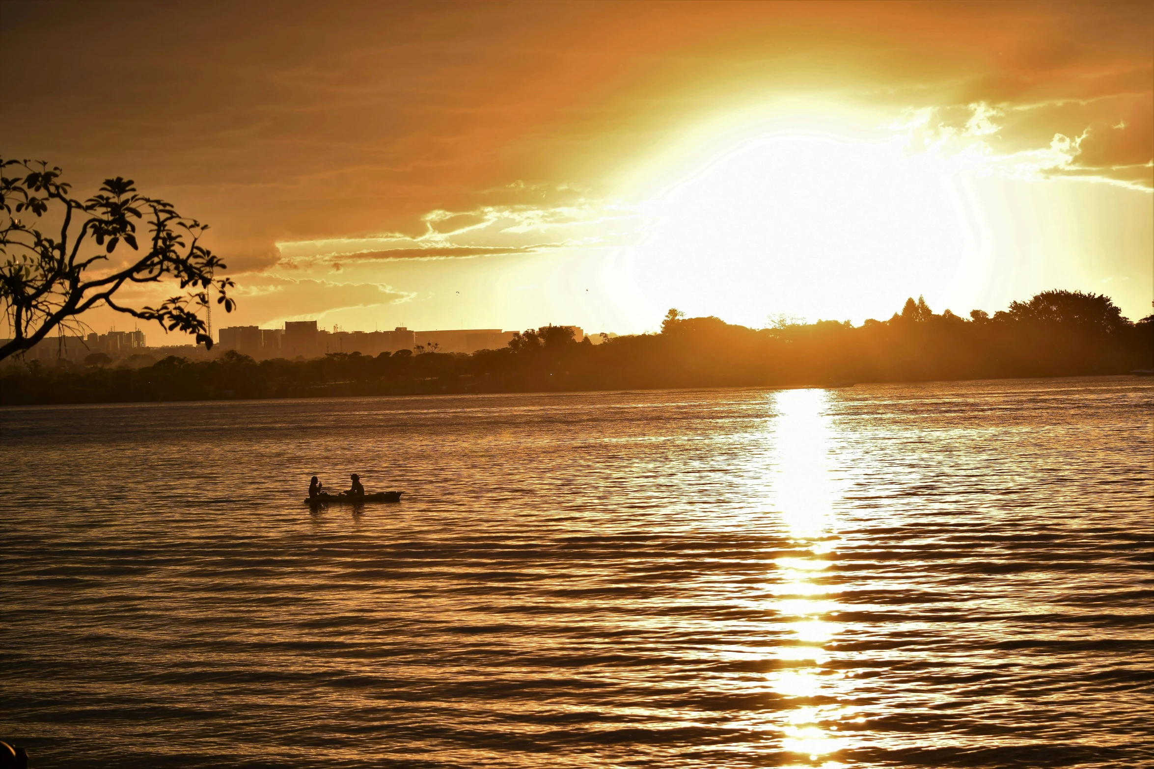 a sun setting over the water and a small boat in it