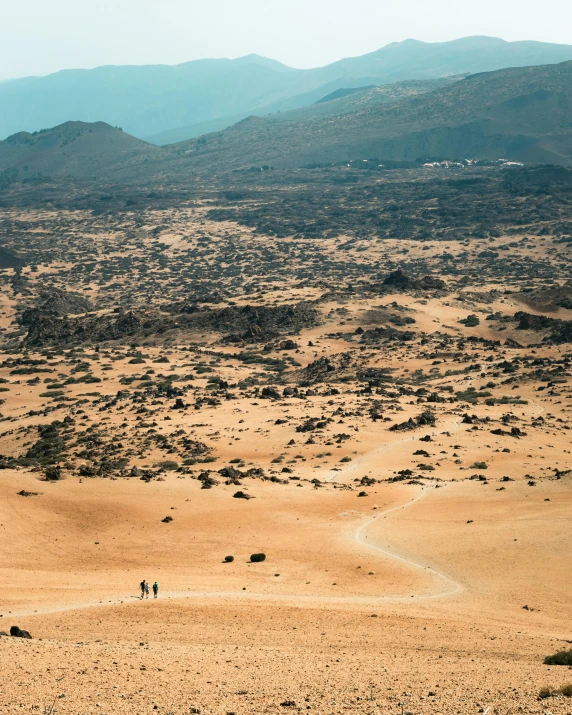 two people walking in the desert with mountains in the background