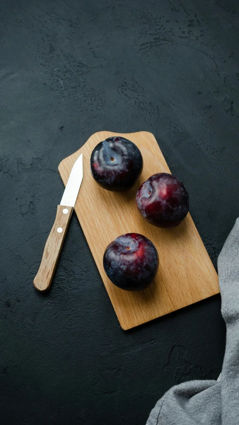 three plums on a  board and a knife