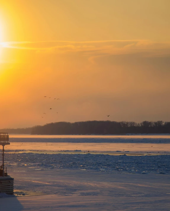 the sun setting over some frozen waters and trees