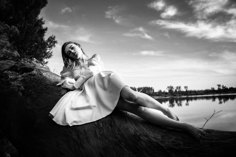 a woman is resting on a tree by the water