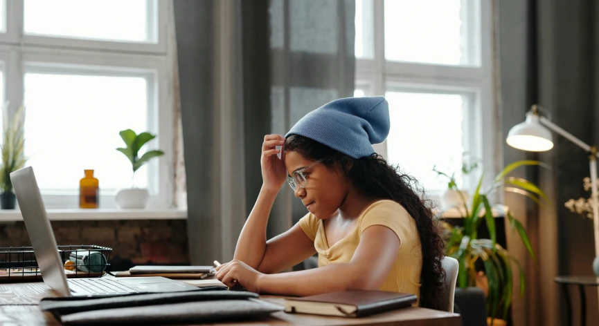 a girl using a laptop computer and wearing a blue beanie