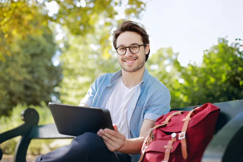 a smiling man sitting on a park bench looking at his tablet