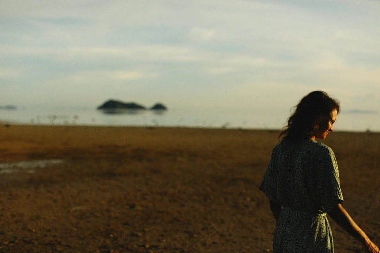 a woman with long hair standing on a beach near the ocean