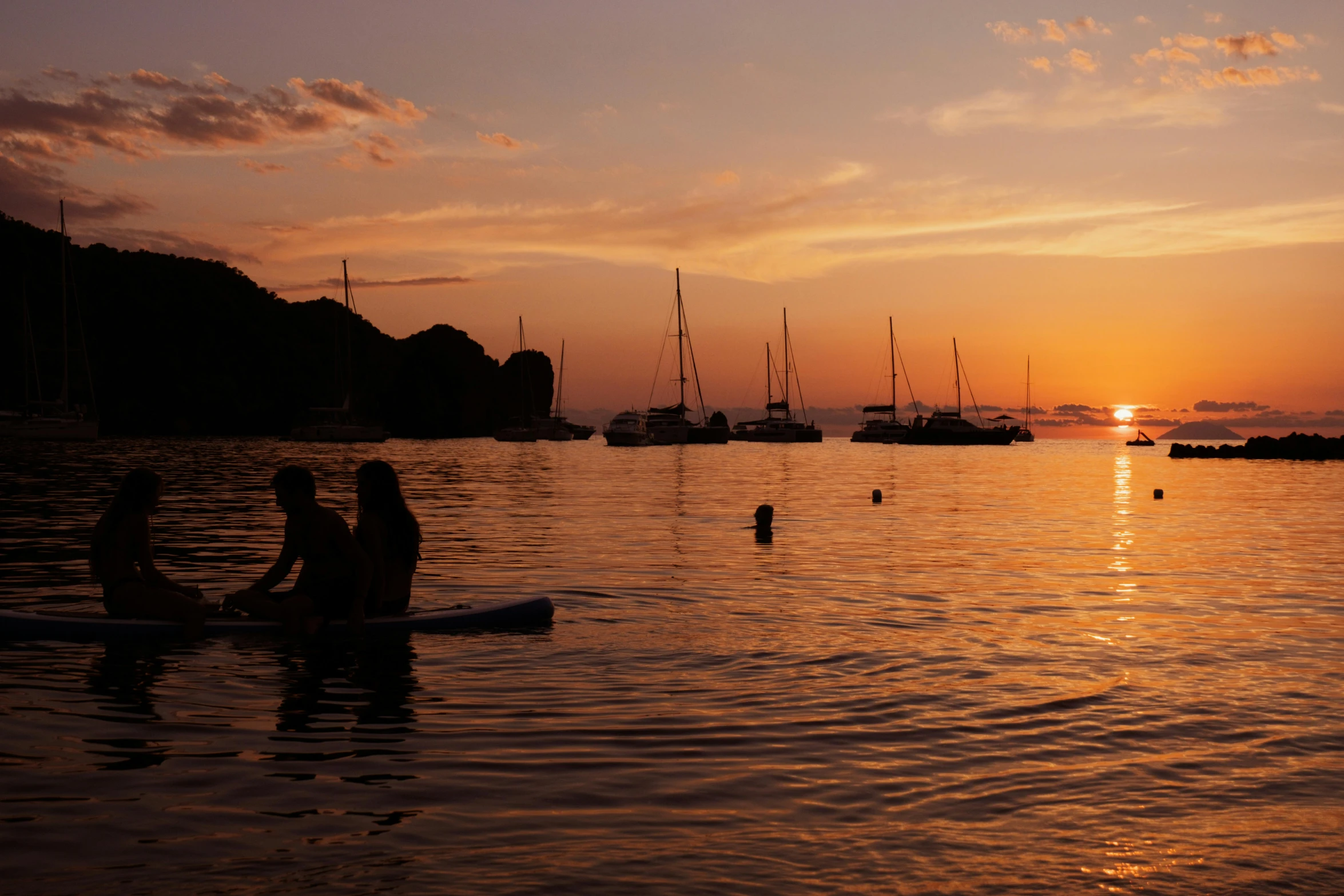 a couple standing on a board in the water with a sunset behind them