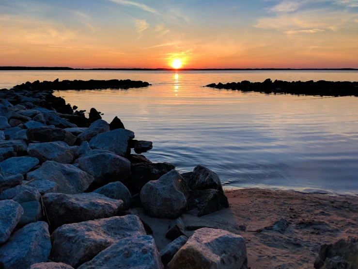 a sunset view of a bay from a shore with rocks on either side