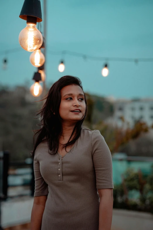 a girl in a dress looks up at some string lights