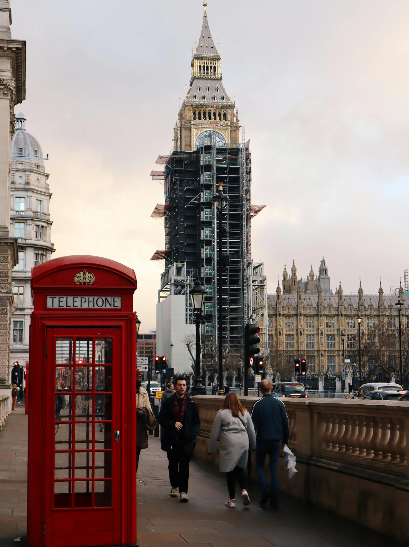 people walk across a bridge that has two red telephone booths