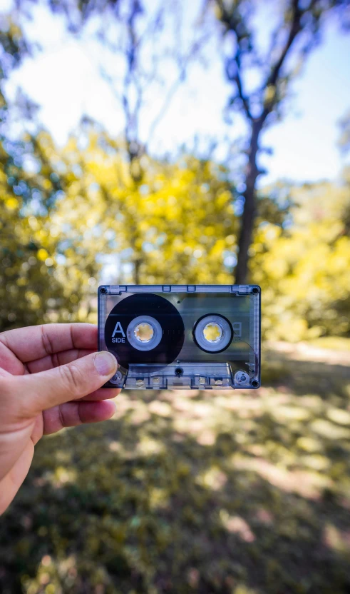 the person is holding up a small cassette with an old school camera attached to it