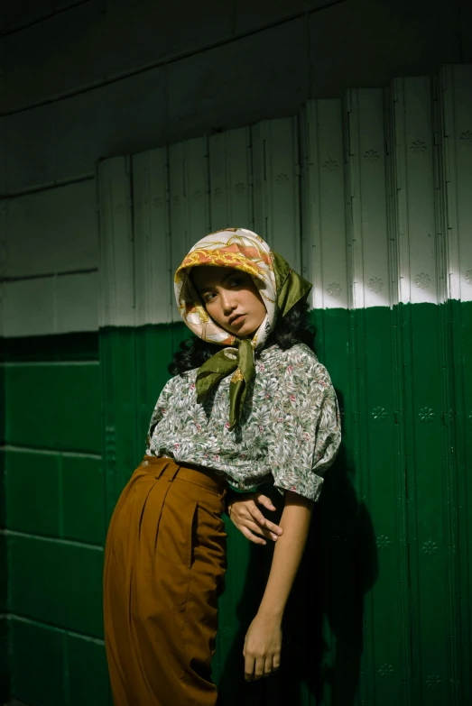 a woman in a sun hat standing against a green wall