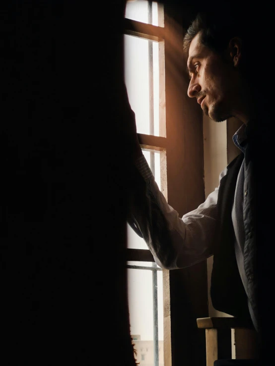 man standing next to window in room and touching his hands