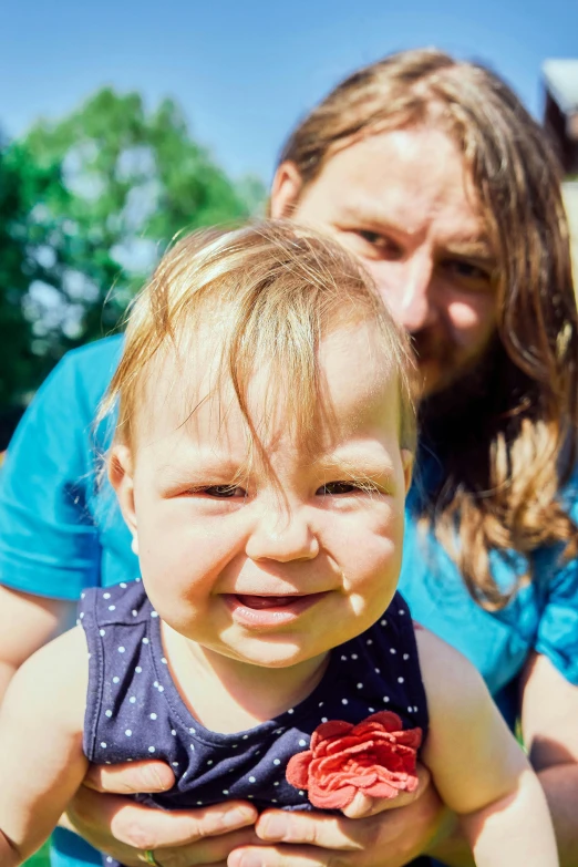 a woman holding up a toddler who is frowning