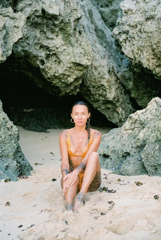 a woman sits in front of some rocks on the beach