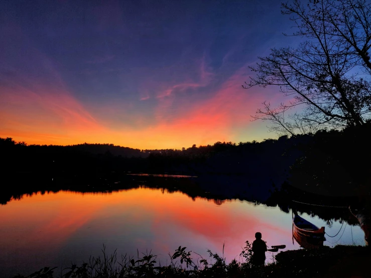 a man sitting in front of a lake under a colorful sky