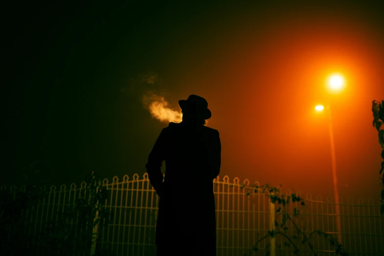 silhouetted man standing against a fence at night
