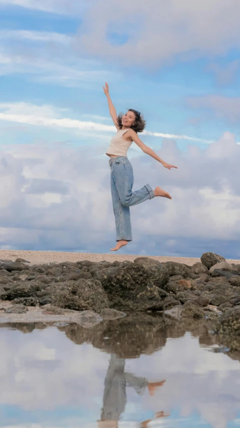 a girl jumps over water from rocks into the ocean