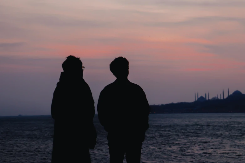 two people standing on a beach in the sunset