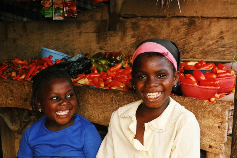 two girls sitting in front of fruit stand