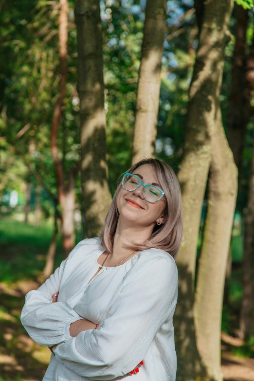 a woman with her arms crossed standing in the woods