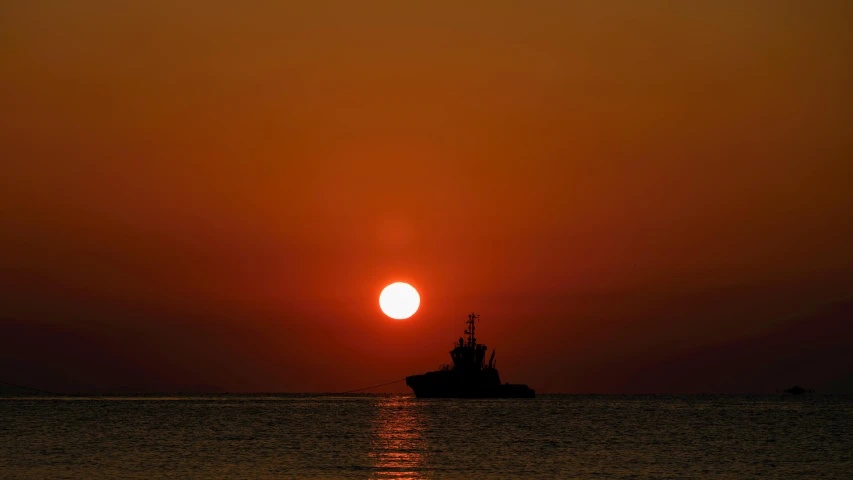 the sun is rising over the ocean with a boat