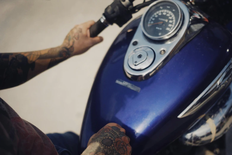 a man with tattoos on his arms stands next to his blue motorcycle