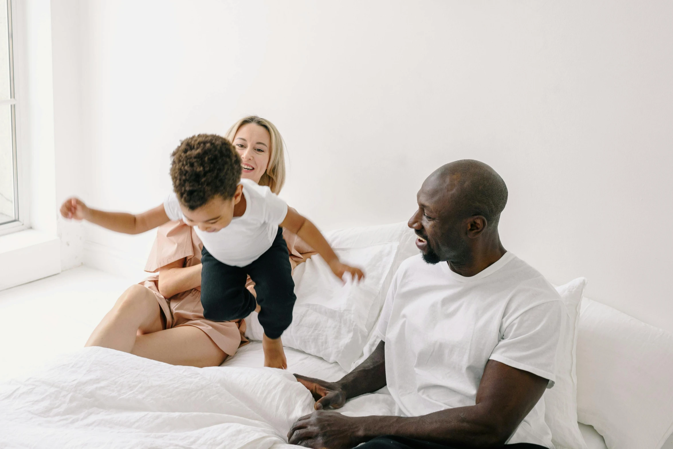 a man and woman sit on a bed playing with a baby