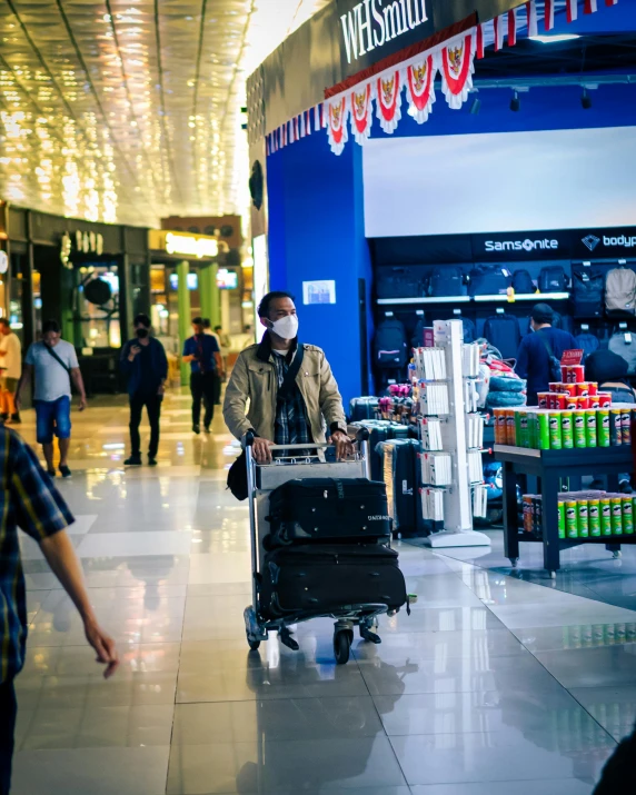 a man wearing a face mask walking while hing a luggage cart