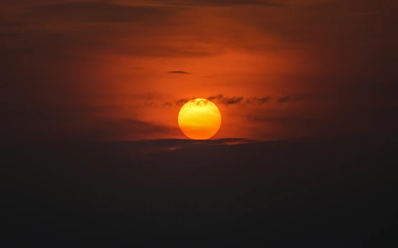 the sun is setting in a cloudy orange sky