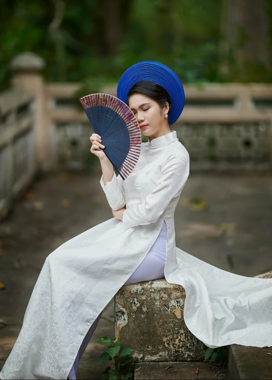 a girl in a white dress and blue hat poses with a fan