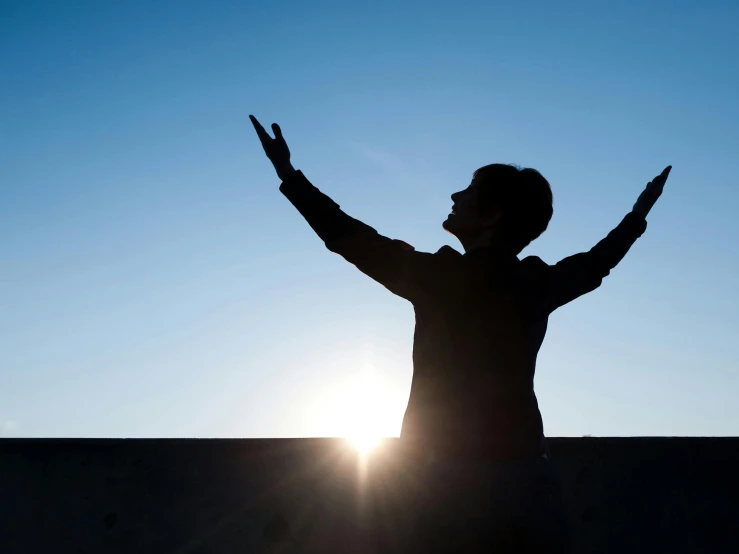 the silhouette of a person raising their arms with one hand