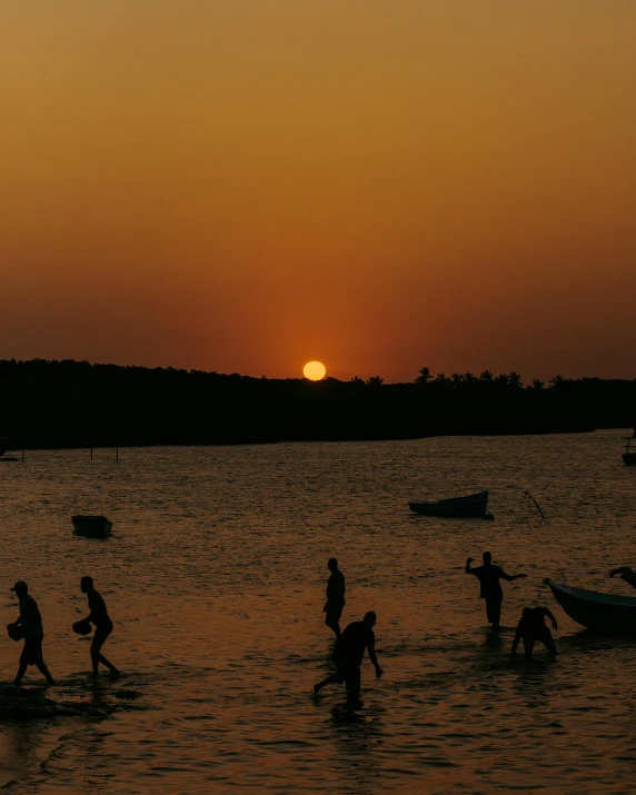 a sunset over a body of water with several people walking in it