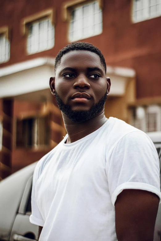 a man stands by a car wearing white t - shirt