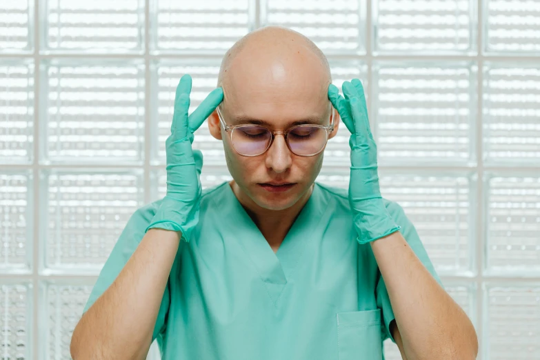 a man wearing green gloves and glasses, holding his hands to his temples