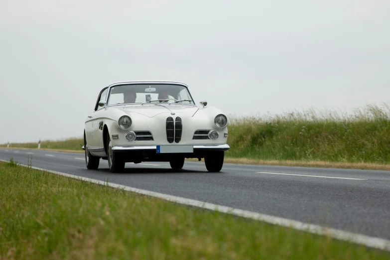 a classic white sports car driving down a winding road