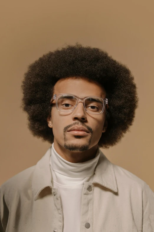 a man wearing glasses and a suit standing in front of a beige wall