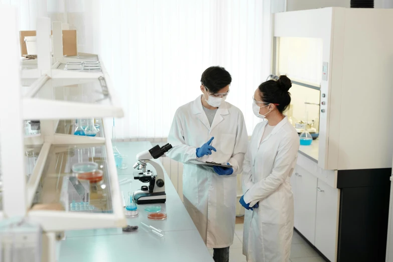 two people wearing white lab coats holding test equipment in a lab