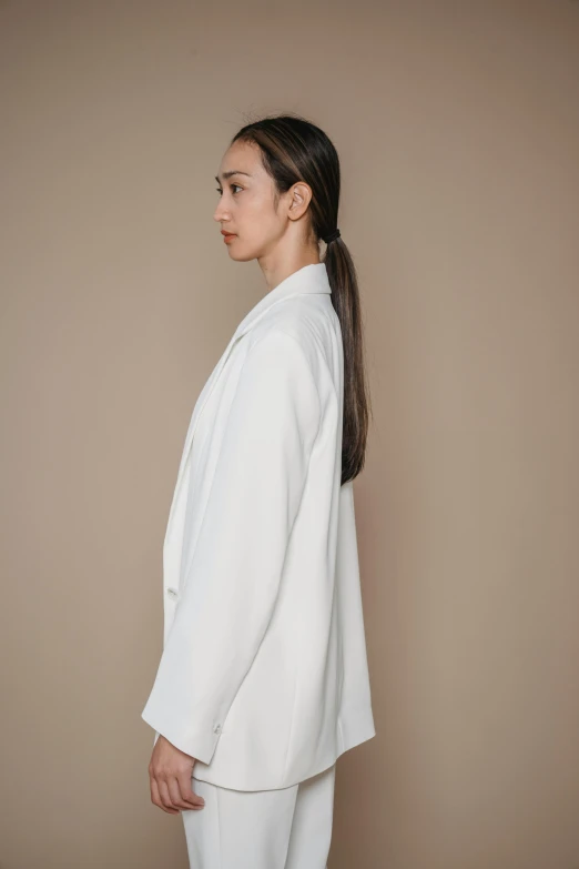 young woman in white blazer and pants standing up with head turned away