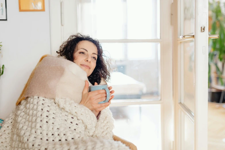the woman is wrapped up in a blanket while drinking her coffee