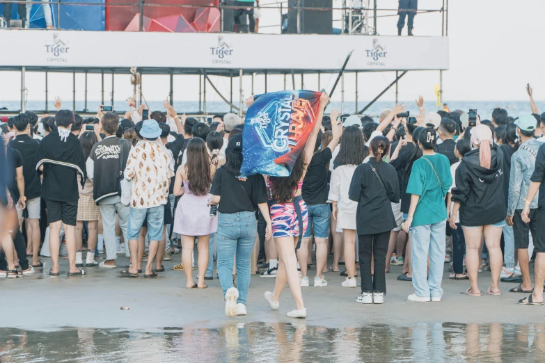 two women hold up a blue kite in front of a large group of people