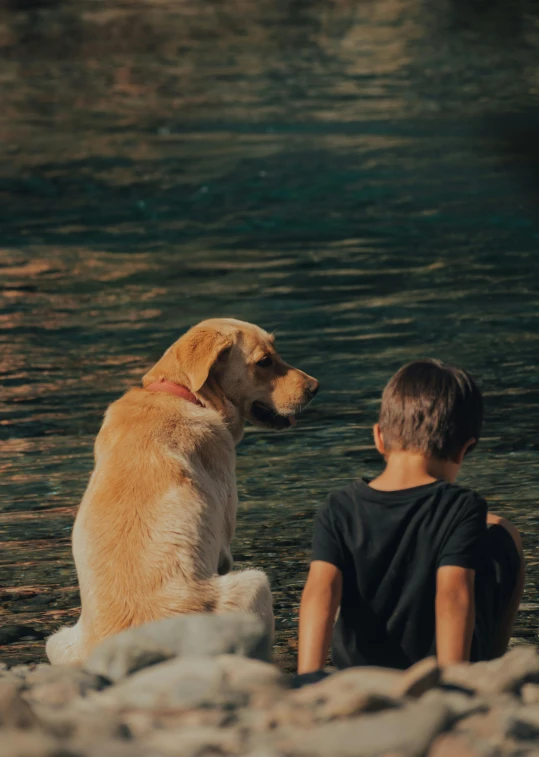 the boy and dog are sitting next to each other on the rocks