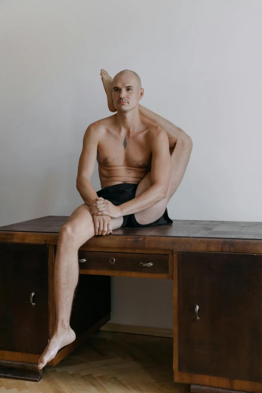 a bald man sits at a desk while his legs are spread across his body