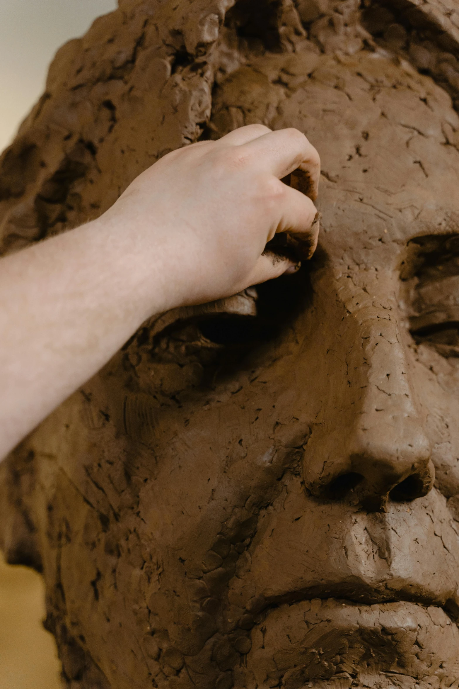 the hand of a woman sculpts a piece of clay on a face