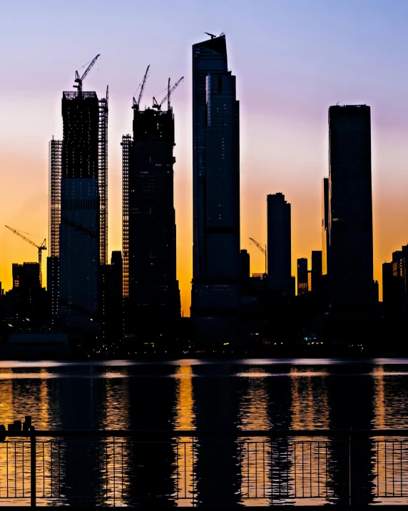 silhouetted city skyline with several tall buildings under construction at sunset