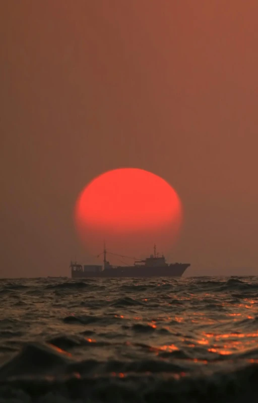 a large red ball floats behind a ship in the ocean