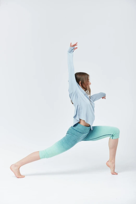 a woman wearing blue shirt and turquoise pants standing in yoga position