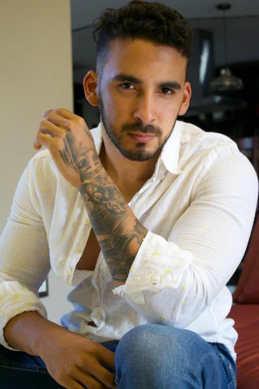 a man with long hair and tattoos sitting in a room