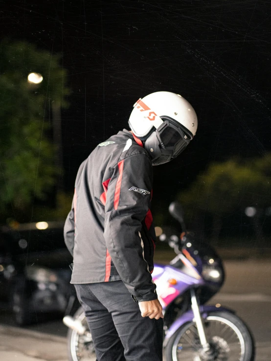 a person in black with a white helmet on standing next to a motorcycle