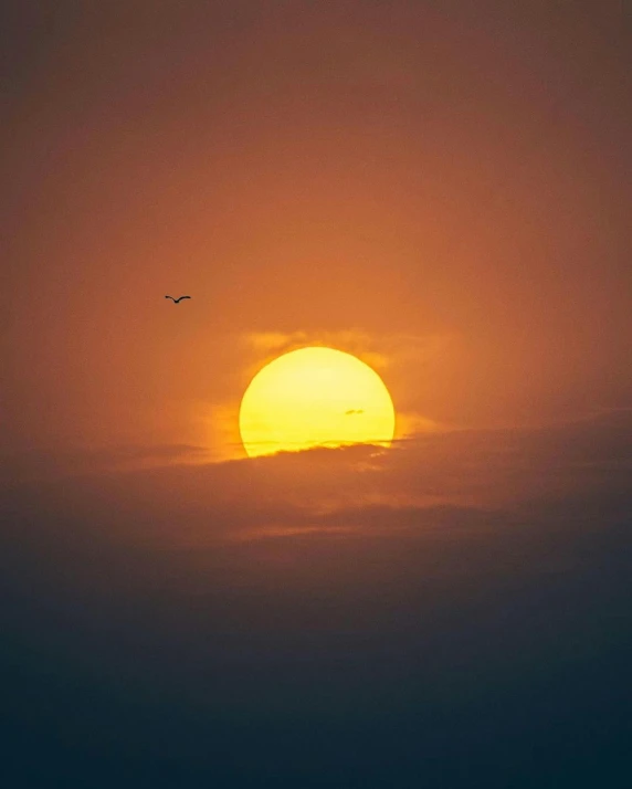 an airplane flies over the setting sun in a cloudy sky