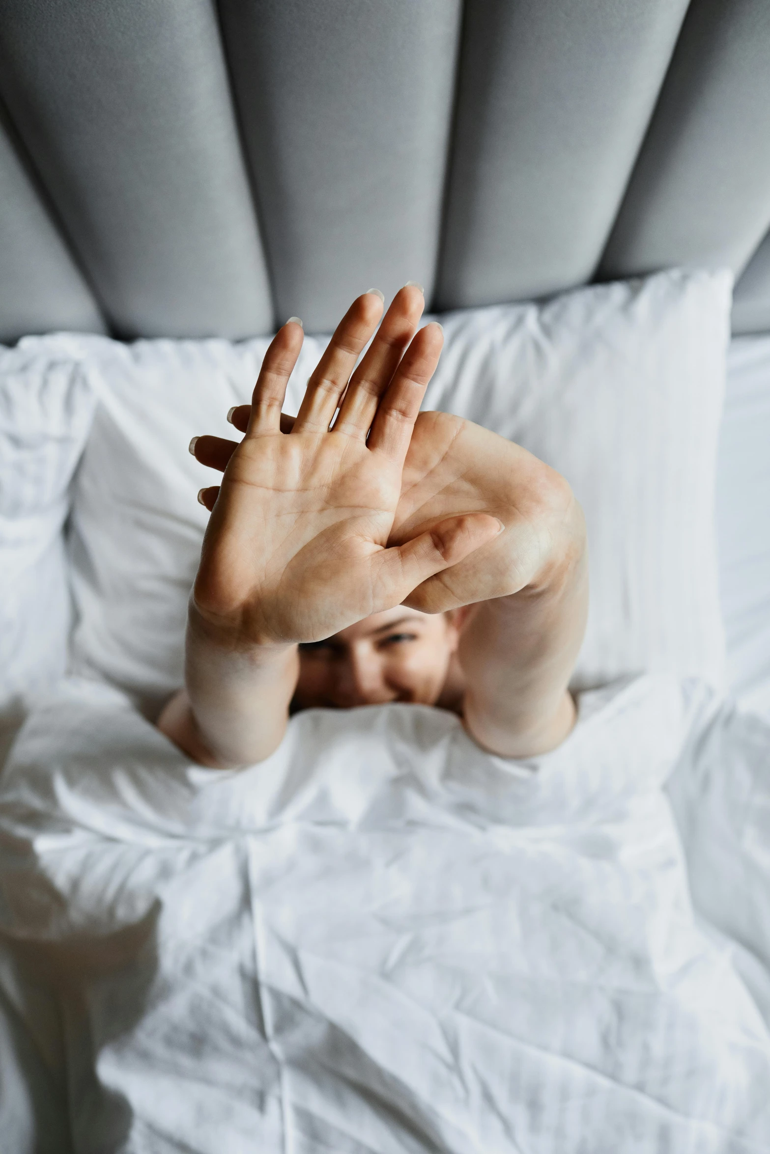 a woman laying in bed covering her eyes and arms with hands