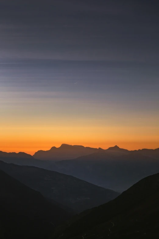 a sunset with mountains and an airplane flying in the sky